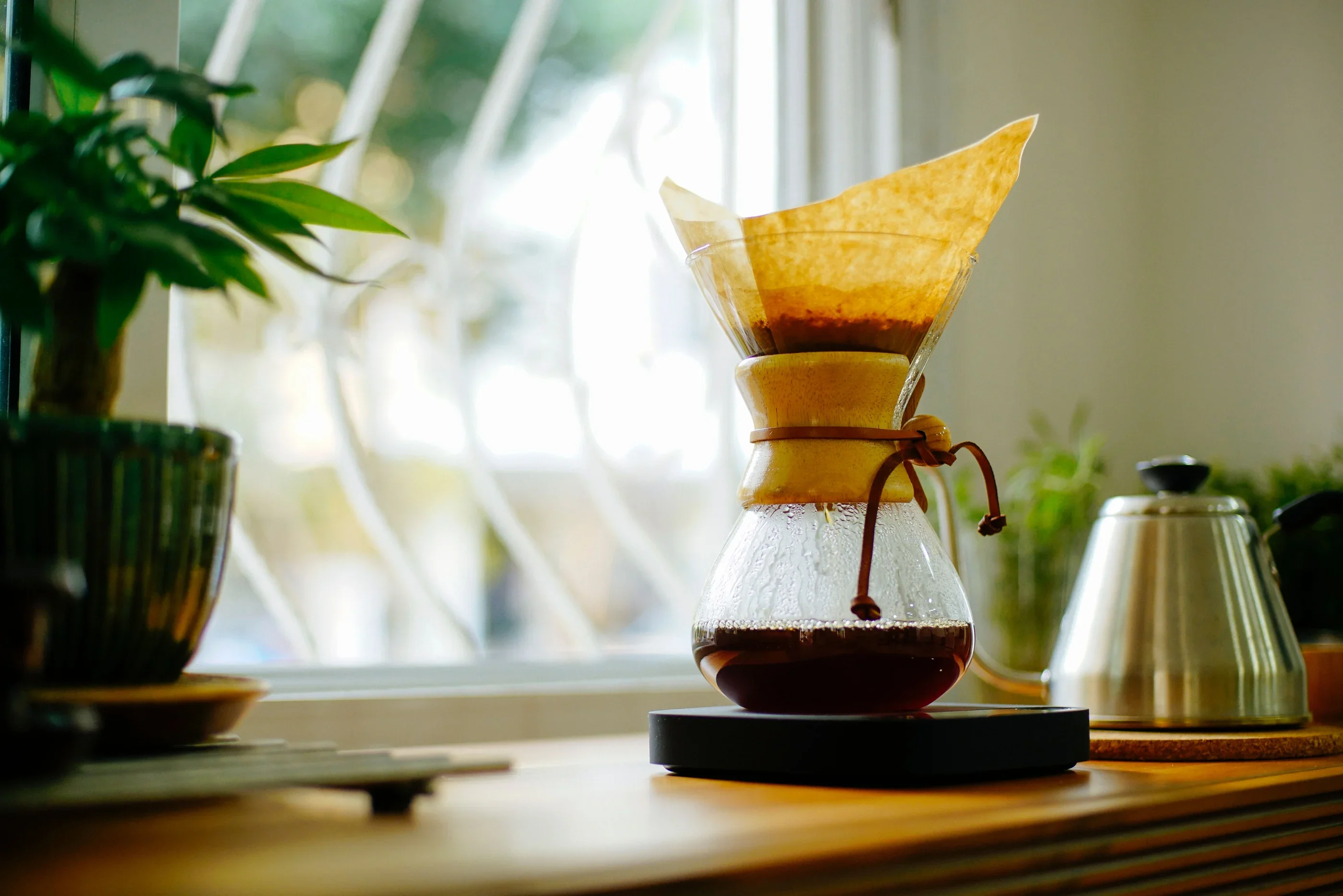 A glass pour-over brewer and kettle in warm window light