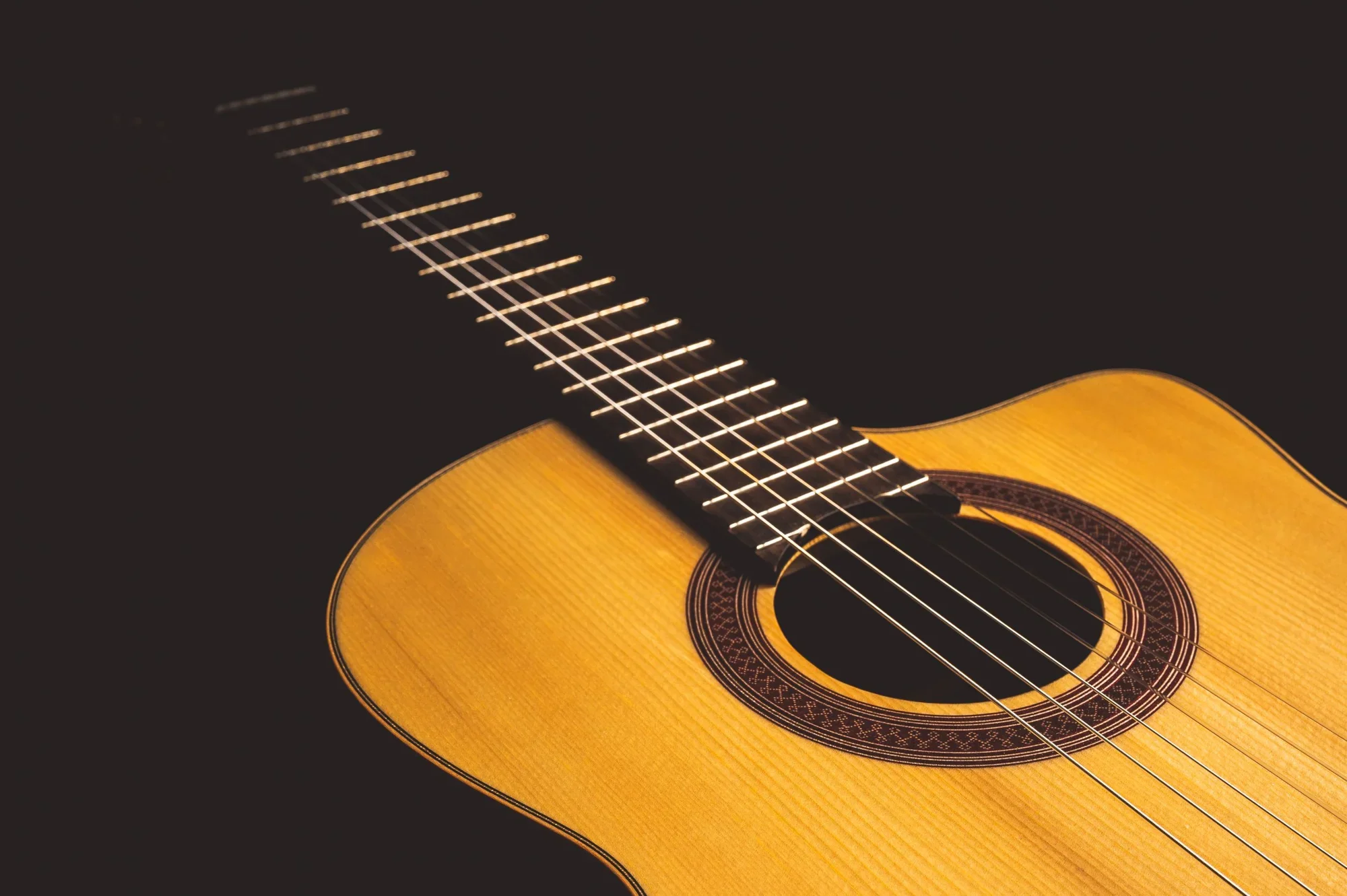 A close view of the classical guitar’s rosette, soundhole, strings, and warm wood
